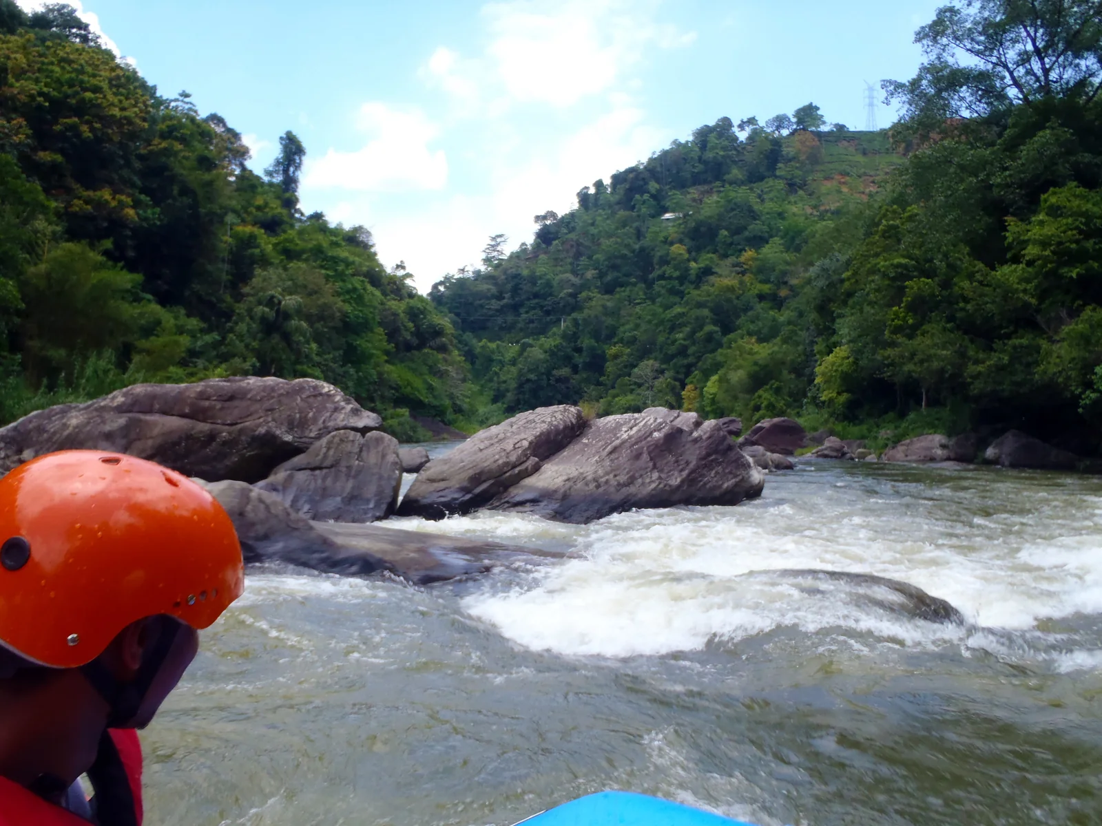 View from a raft towards white-water rapids and rocks at Kitulgala, with a helmeted rafter in the foreground.